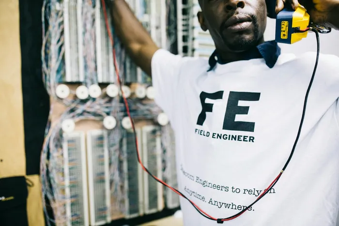 A technician in a white shirt with 'FE' printed on it, managing network cables and equipment, indicative of field engineering work in technology settings.